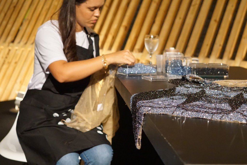 Uma bordadeira mostra o trabalho paciente que é bordar estes vestidos.